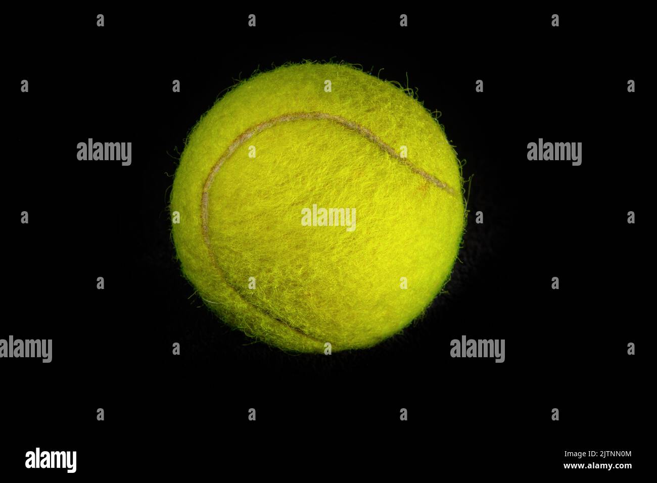 Fuzzy yellow tennis ball photographed in closeup detail against a dark