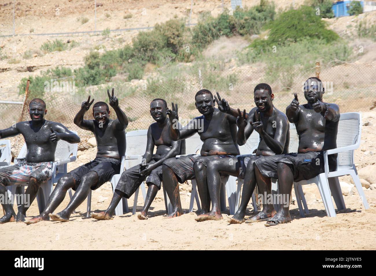 DEAD SEA, JORDAN: APRIL, 18, 2014. a group of African young men taking mud bath in the sun at the beach of Dead Sea. Stock Photo