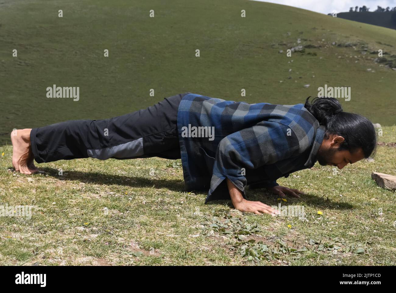 Full length side view of a handsome long haired Indian young man doing push ups in the mountain Stock Photo