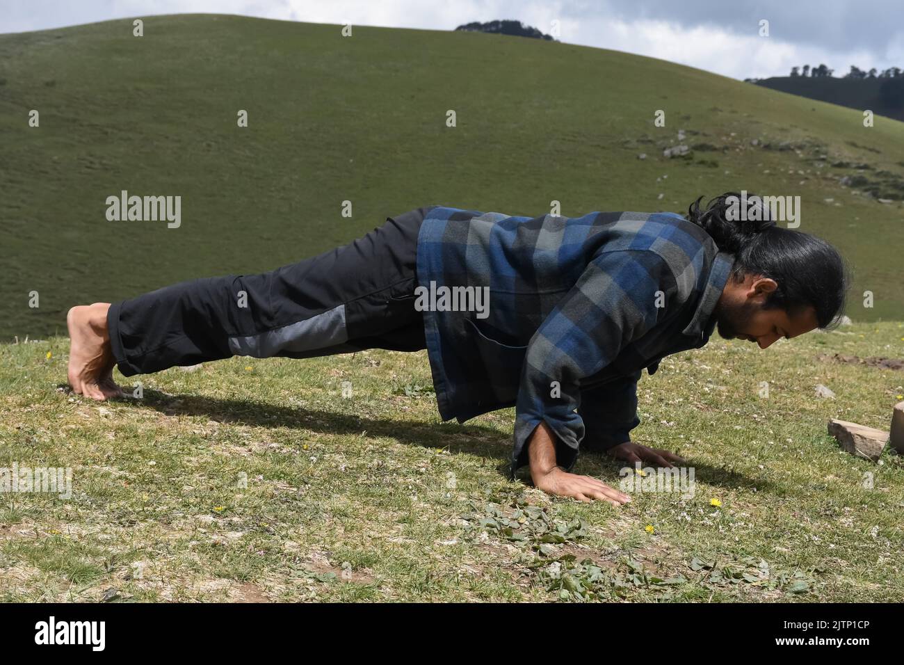 Full length side view of a handsome long haired Indian young man doing push ups in the mountain Stock Photo