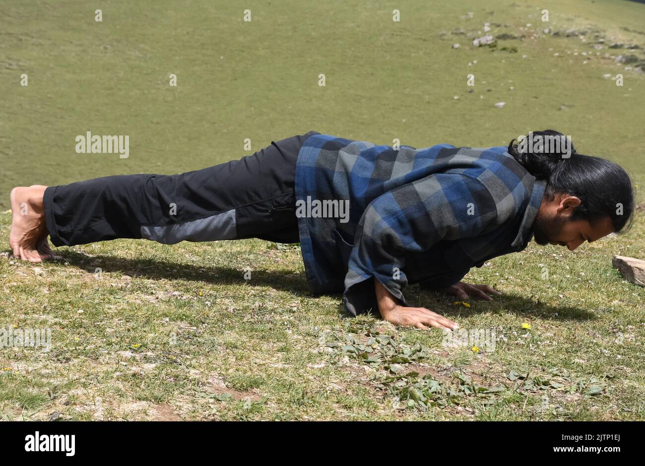 Full length side view of a Indian young man with ponytail hair style doing push-ups in the mountain Stock Photo