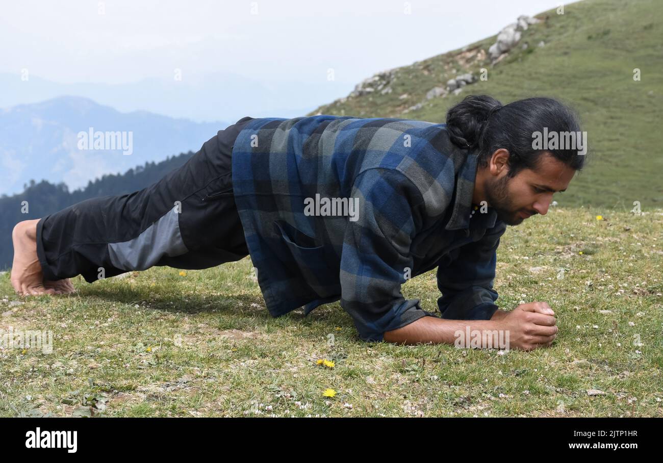 Full length of a handsome Indian young man with ponytail hair doing plank exercise in the top of mountain Stock Photo