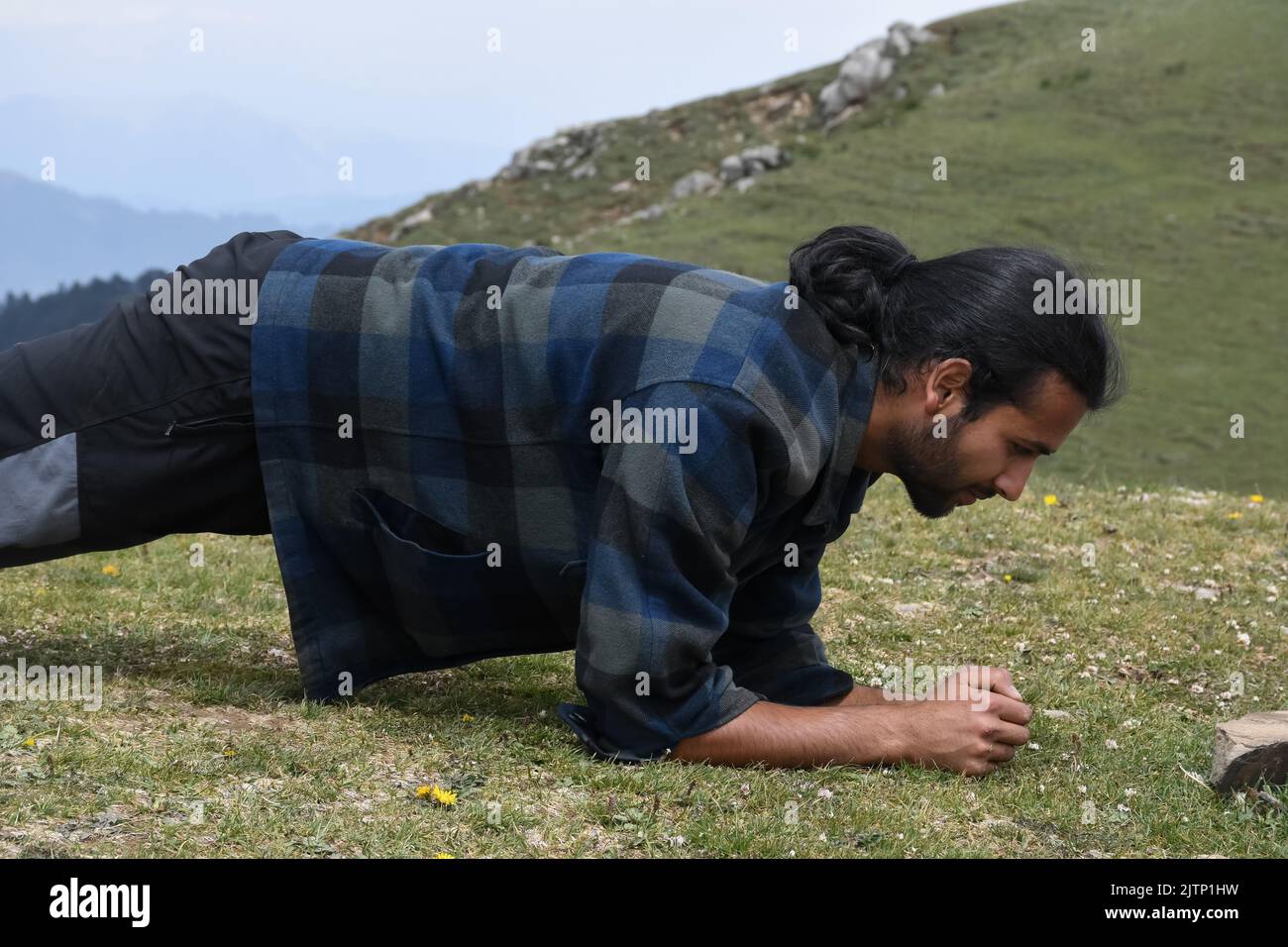 Side view of a handsome young Indian man with ponytail hair doing plank exercise in the mountain Stock Photo