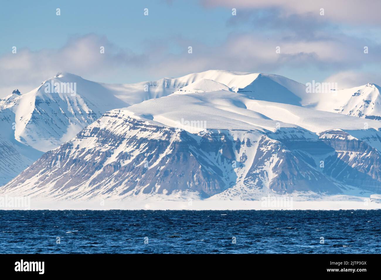 The pristine snow covered mountains of Svalbard, a Norwegian archipelago between mainland Norway and the North Pole, and the cold blue waters of a fjo Stock Photo