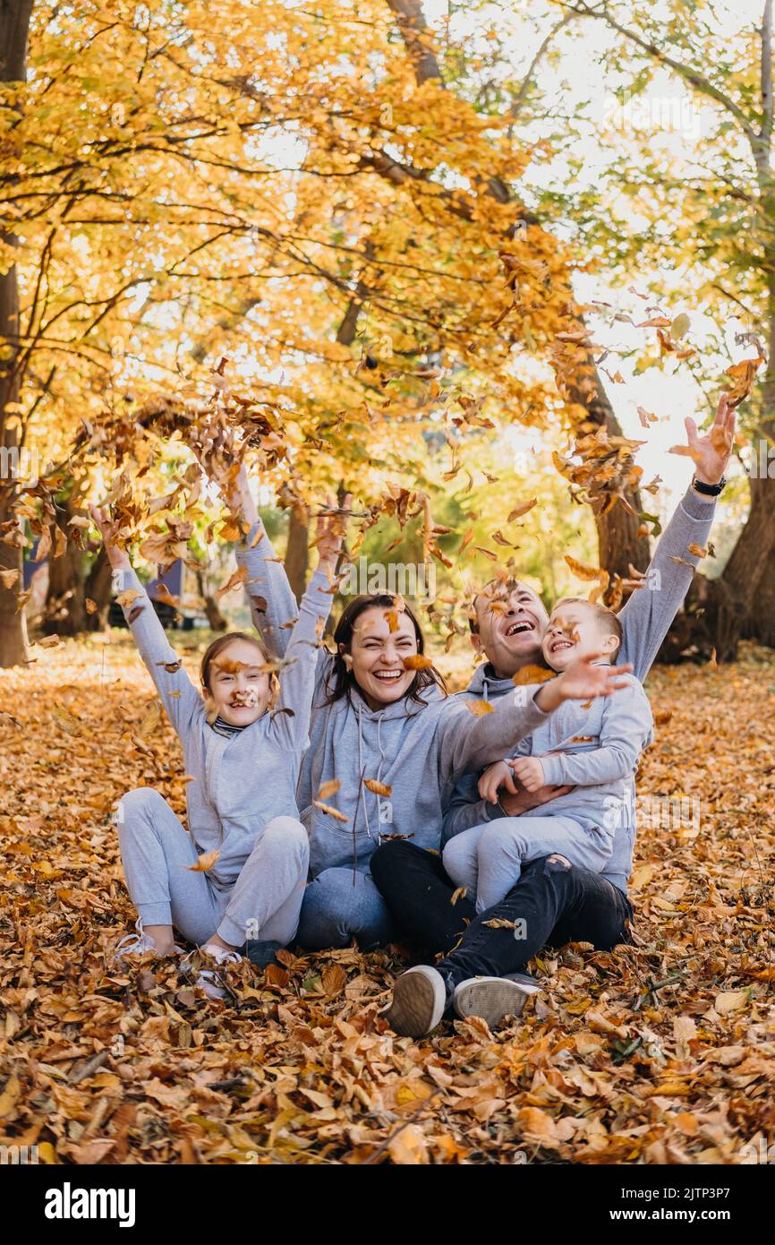 Portrait of a family taking group photos while happily throwing dry leaves of different colours in the air, spending time together during autumn Stock Photo