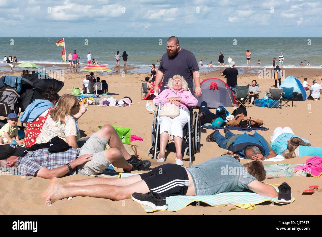 Old lady in wheelchair sunbathing with family at Sandy beach in Botany