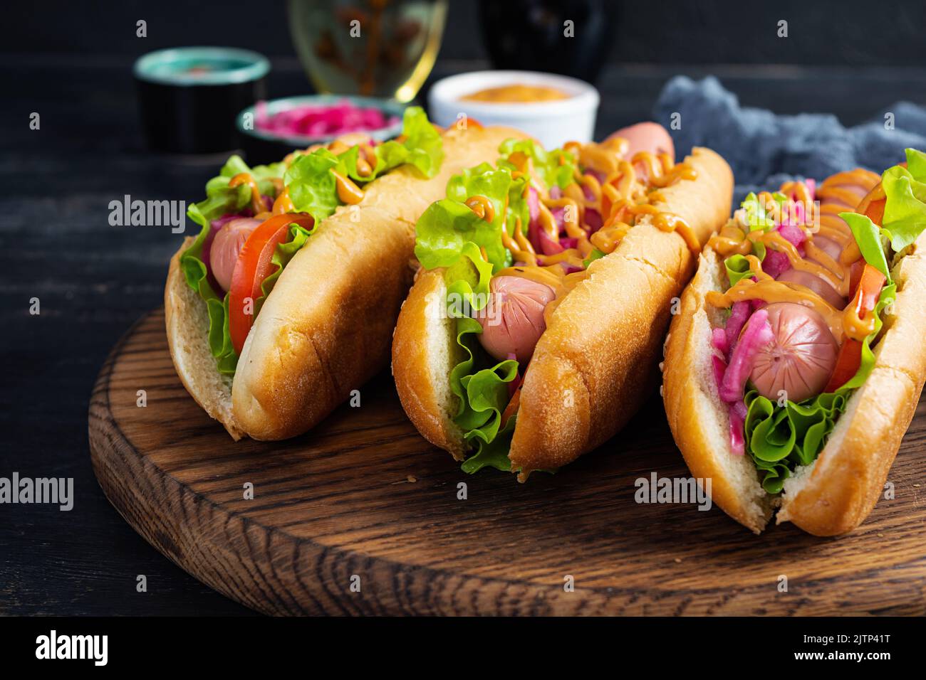 Hot dog with lettuce, tomatoes and pickled onions. Grilled bun with