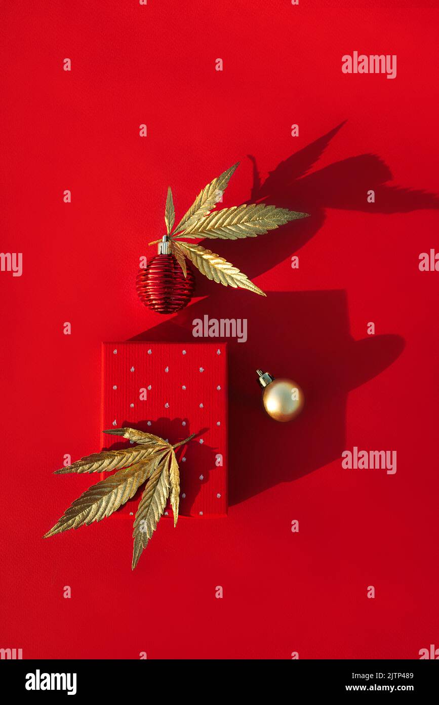 Red gift box, golden Christmas balls and golden leaves of marijuana on a red background. Stylish background for New Year's, Christmas sales and promot Stock Photo