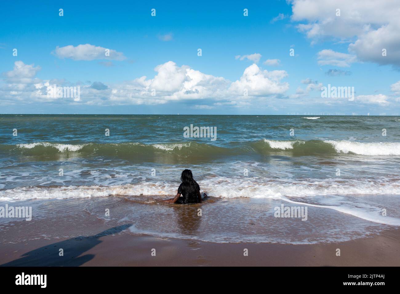 Young child in dark clothing sitting in the waves Stock Photo