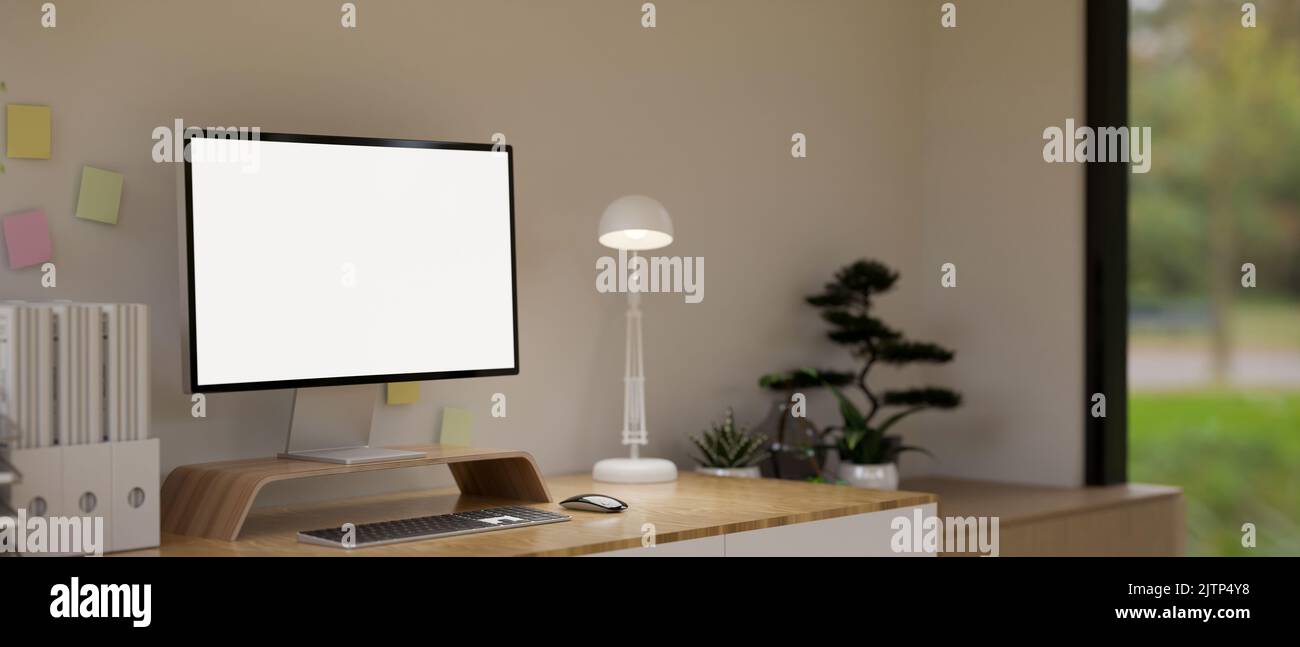 Minimal cozy home office interior design with white screen computer mockup, table lamp, office supplies, decor plants and decor on wood table over whi Stock Photo
