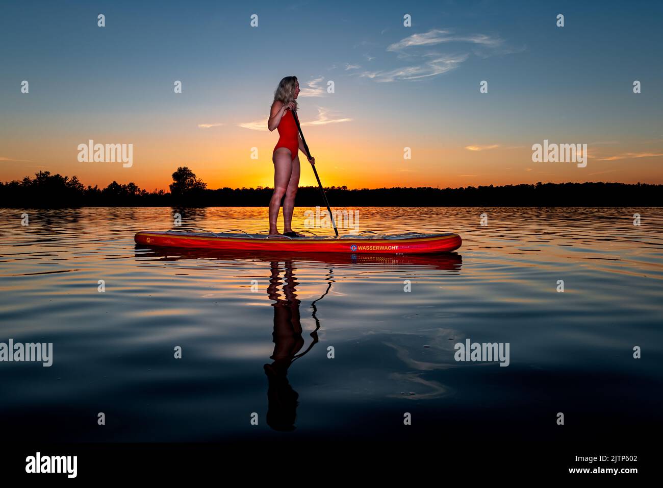 Water rescue on a Stand Up Paddling board in front of the setting sun. Stock Photo