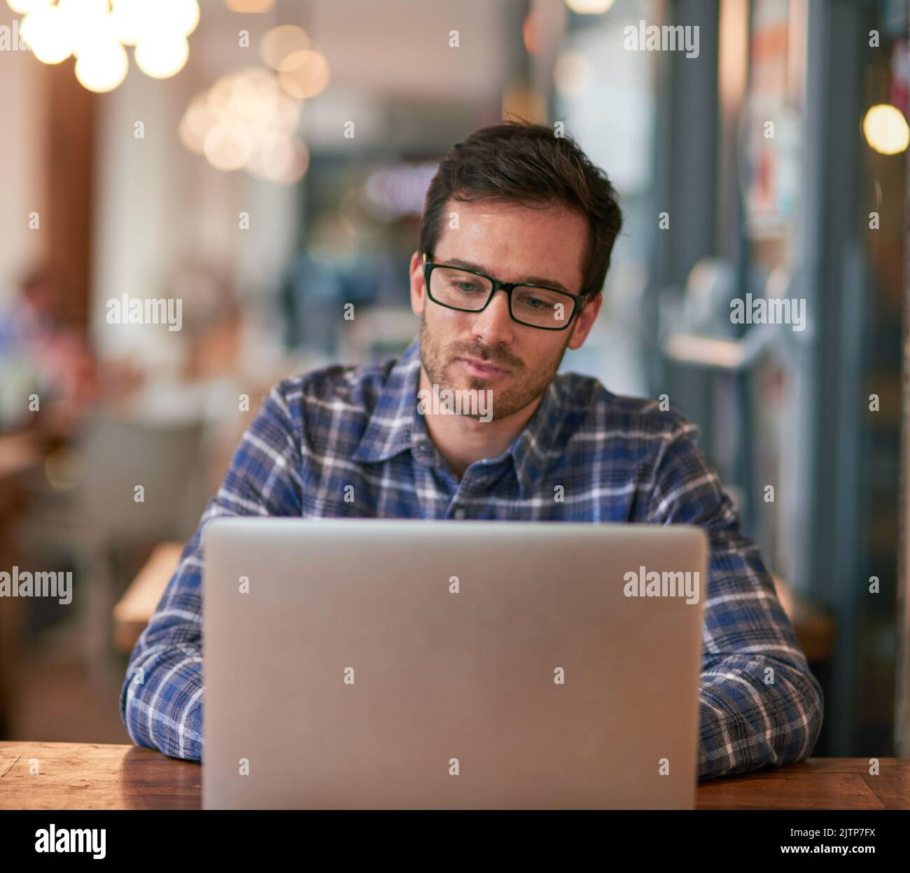 Free wifi available here - bring your laptop. a young man using his laptop while sitting in a coffee shop. Stock Photo