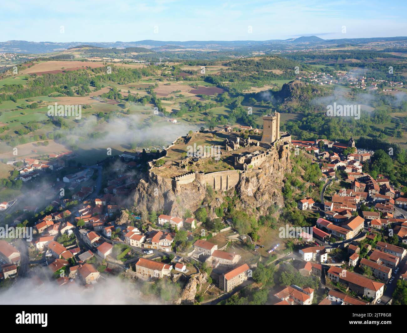 AERIAL VIEW. Fortress of Polignac, on a basaltic mesa with the low-lying morning fog. Polignac, Haute-Loire, Auvergne-Rhône-Alpes, France. Stock Photo