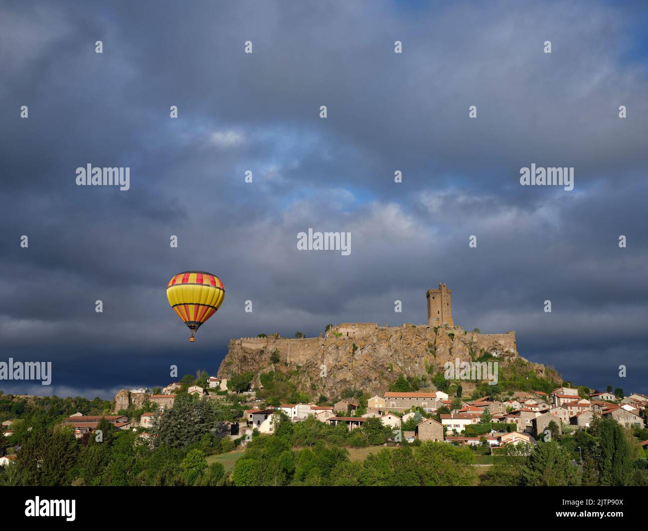 Hot air balloon drifting near a medieval fortress on a volcanic mesa. Polignac, Haute-Loire, Auvergne-Rhône-Alpes, France. Stock Photo