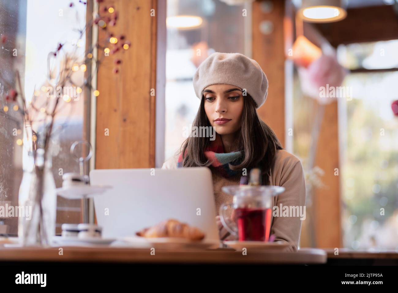 Shot of cheerful beautiful woman sitting inside a coffee shop and using ...