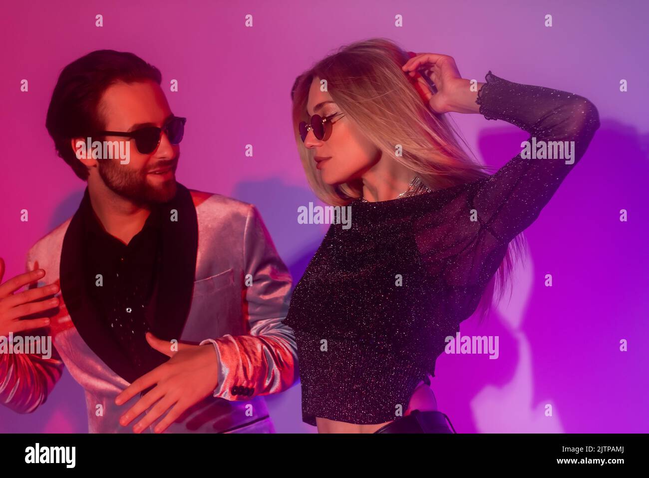 Stylish couple in sunglasses dancing during party on purple background Stock Photo Alamy