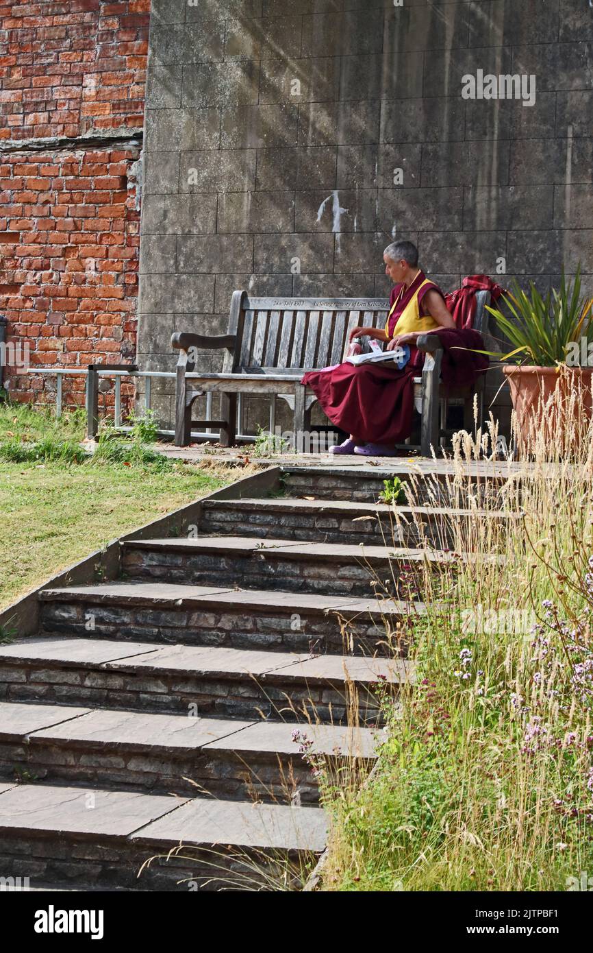 Lady in buddhist robes sat on bench in sunshine Stock Photo