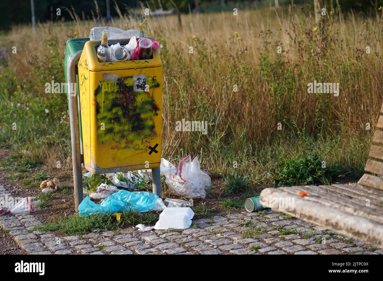 overflowing garbage can with garbage lying next to it in a park on a summer day Stock Photo