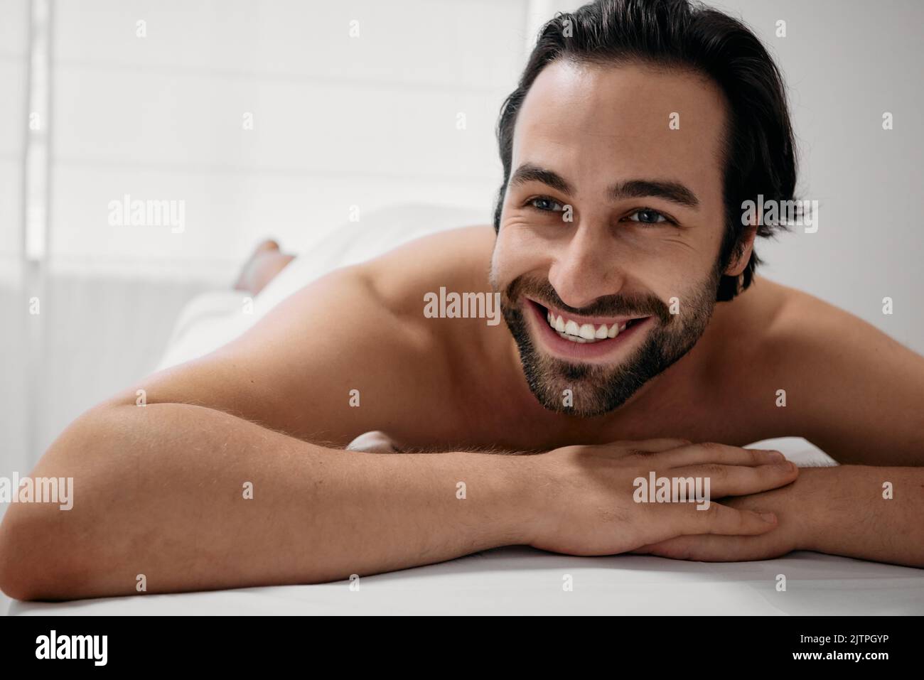 Weekend on wellness spa. Portrait of happy man with toothy smile lying on massage table after relaxes anti-stress massage Stock Photo
