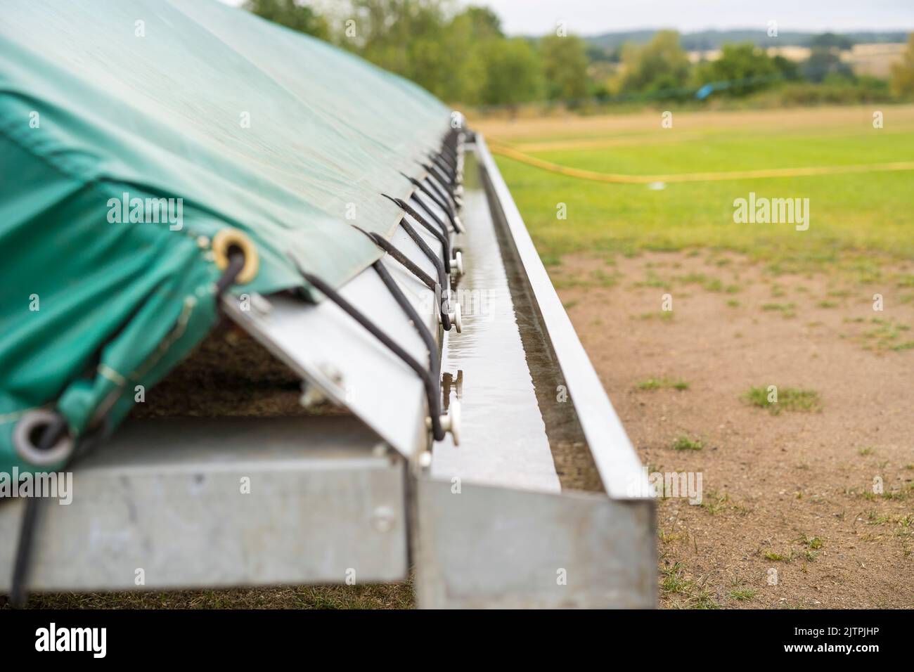 Closeup end view of a cricket pitch cover showing the drainage channel