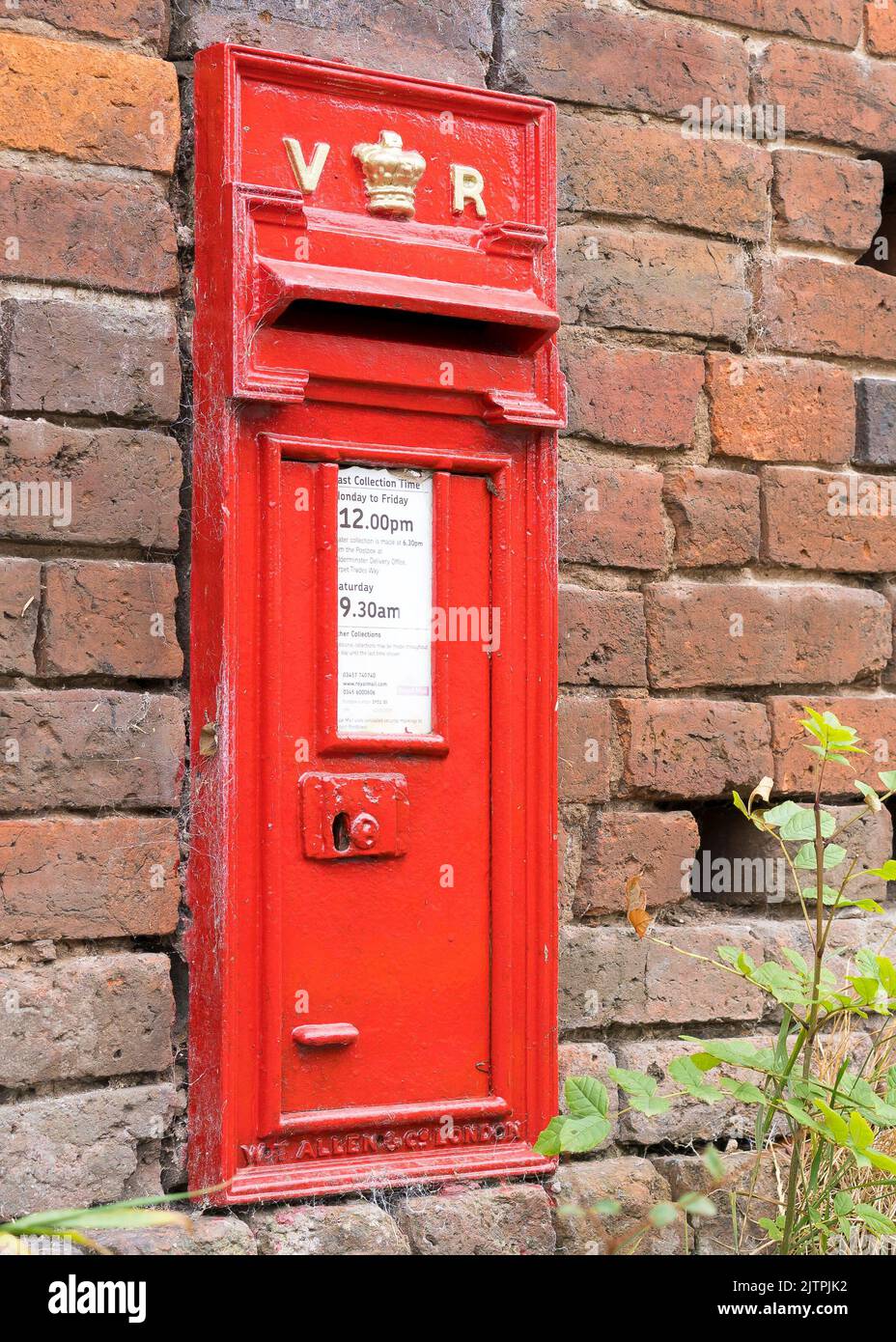 Close up of Victoria Regina red post box set in old brick wall in rural English village. The UK postal service vintage letter boxes still in use today. Stock Photo