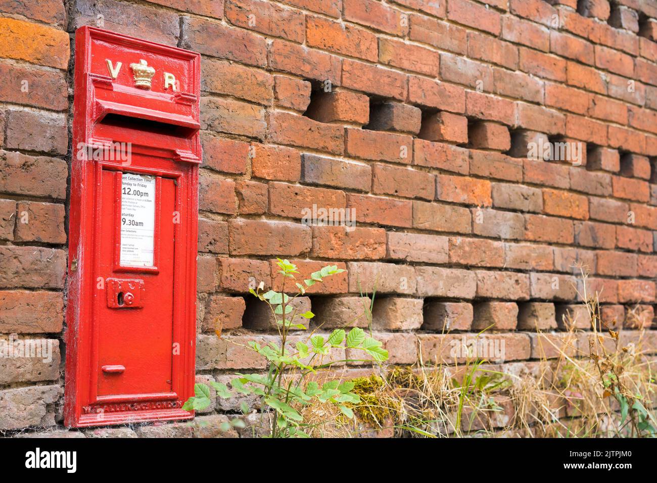 Close up of vintage Victoria Regina red post box (still in use by Post Office/Royal Mail) set in an old brick wall in UK rural village. Stock Photo