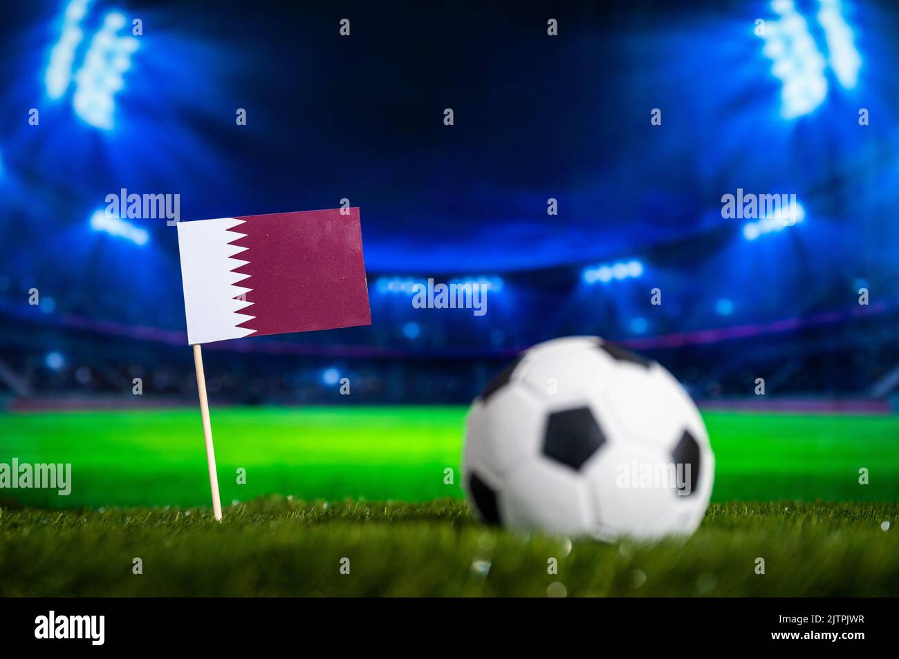 Qatar Mini Flag and football ball. Sport soccer Wallpaper. Football Stadium in night in Background Stock Photo