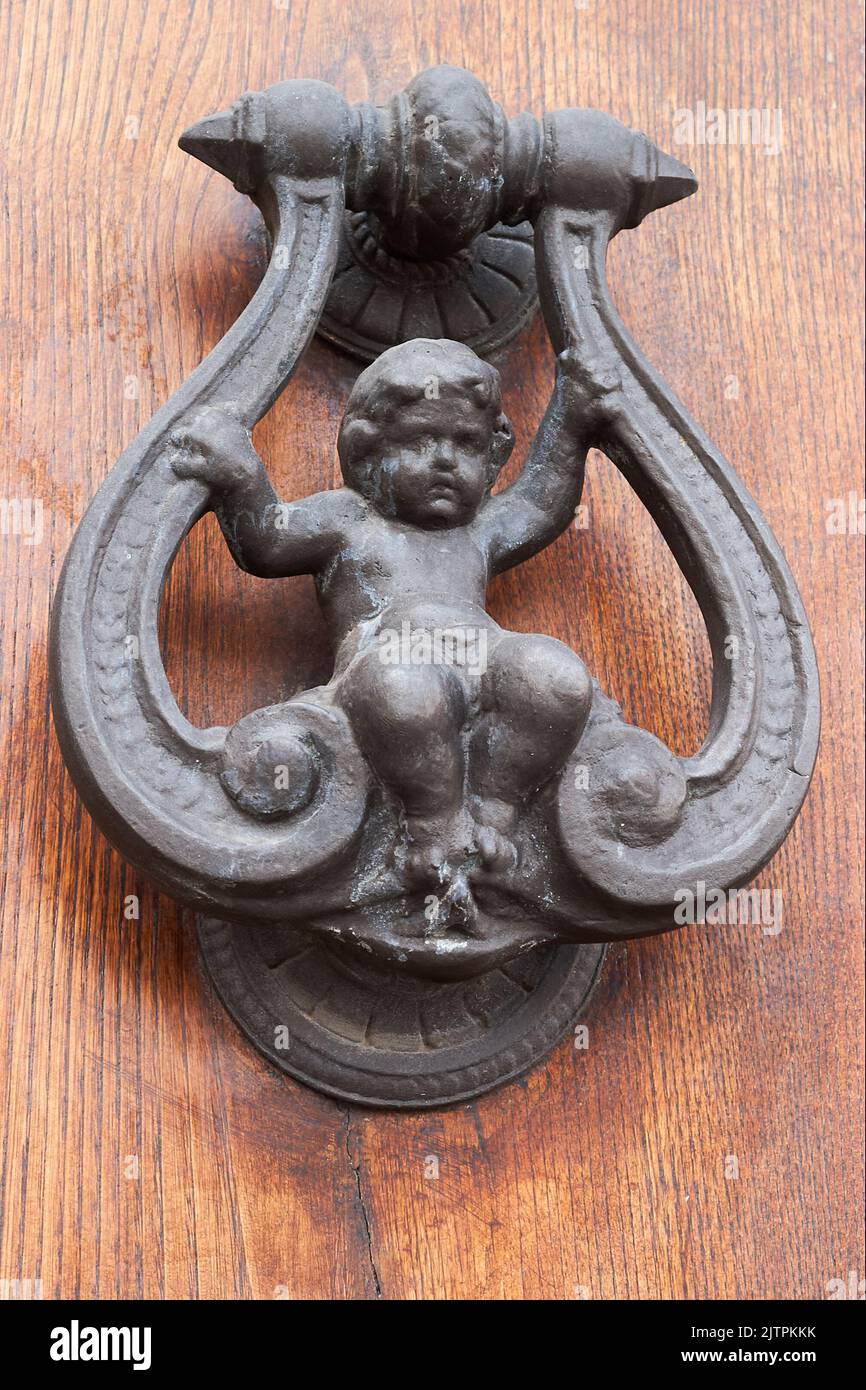 Old wrought iron knocker representing a child sitting on a swing on a wooden door Stock Photo