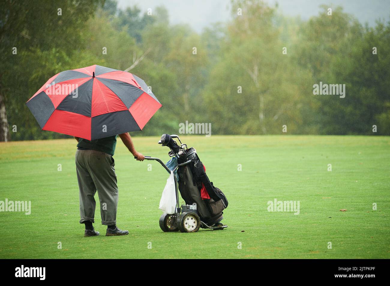 Man with colorist umbrella and electric golf cart under rain in the golf course Stock Photo
