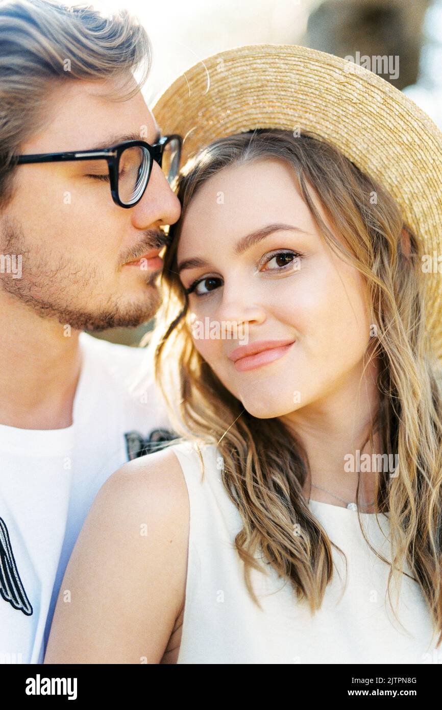 Man in glasses touches his lips the forehead of a smiling woman ...