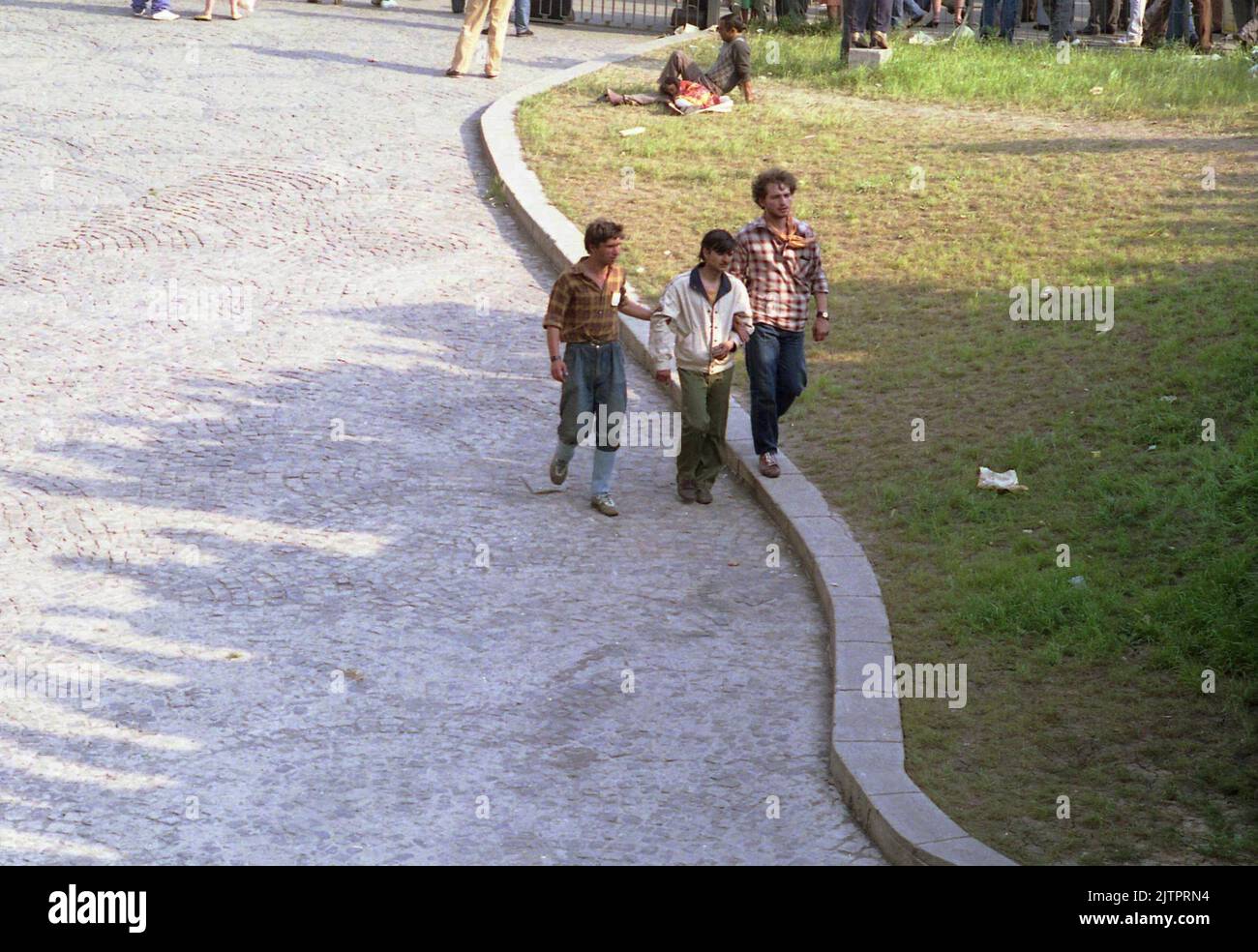 Bucharest, Romania, April 1990. A few months after the anti-communist revolution, sign of poverty and struggle were still seen anywhere. Here, an intoxicated man is helped by two others to walk. Stock Photo