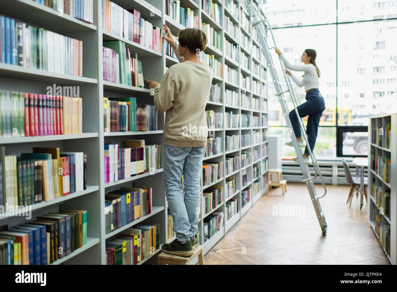 full length of teenage students choosing books on racks in library ...