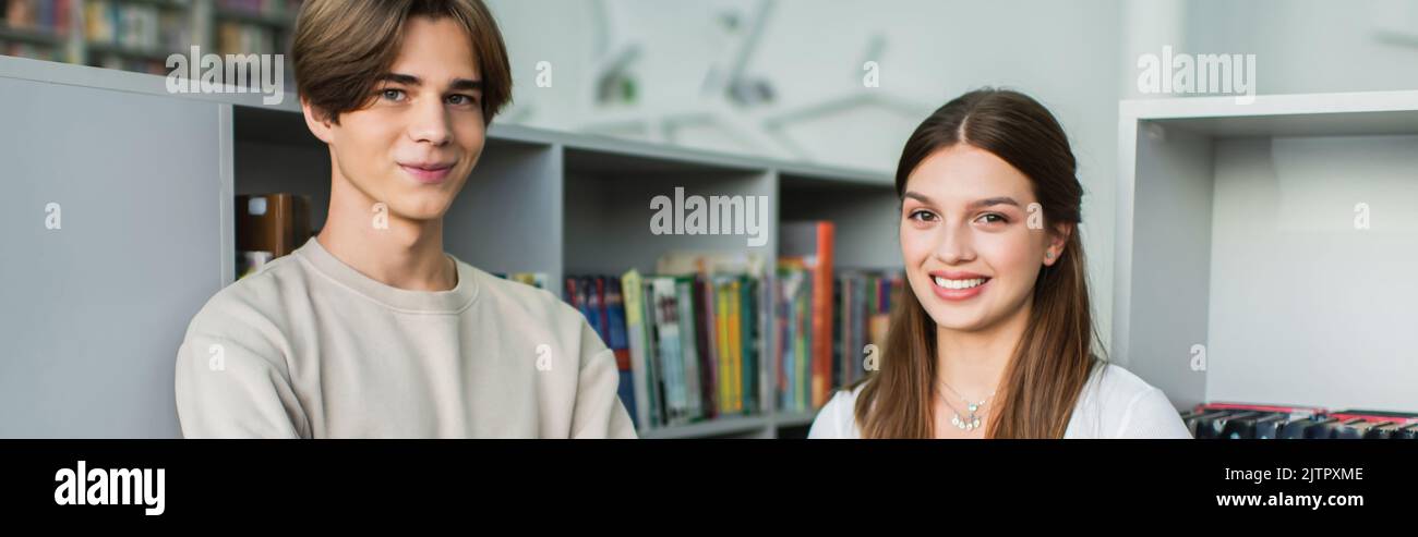 happy teenage students looking at camera near bookshelves in library, banner,stock image Stock Photo