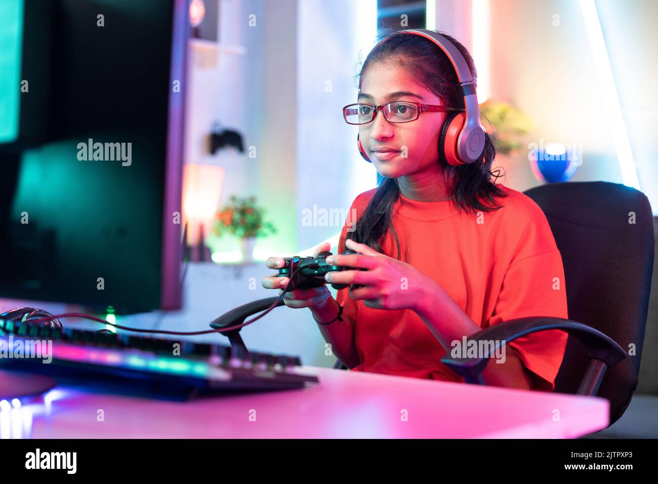 girl kid with wireless headset playing online video game on computer using joystick at home - concept of entertainment, gaming addiction and Stock Photo