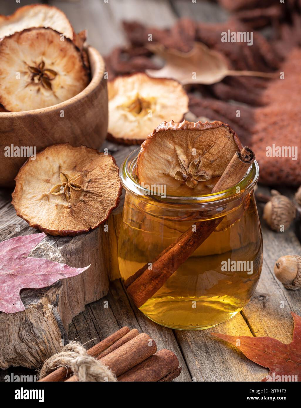 Glass of apple cider with cinnamon stick and dried apple chips on rustic wooden table Stock Photo