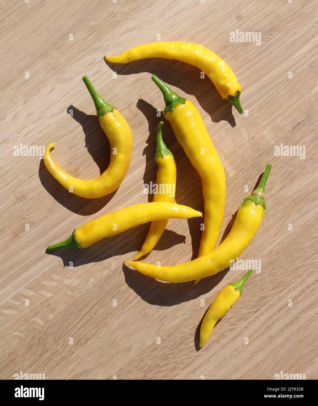 A Pile of Bright Yellow Cayenne Peppers on a Light Wood Background Stock Photo