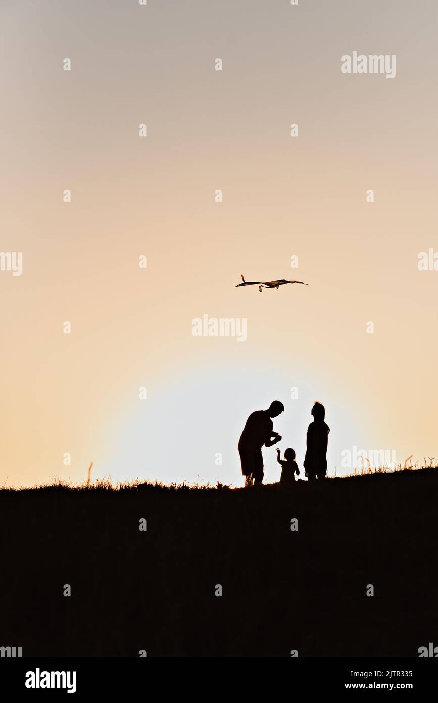 Silhouettes of a family mom, dad and daughter flying a kite at sunset ...