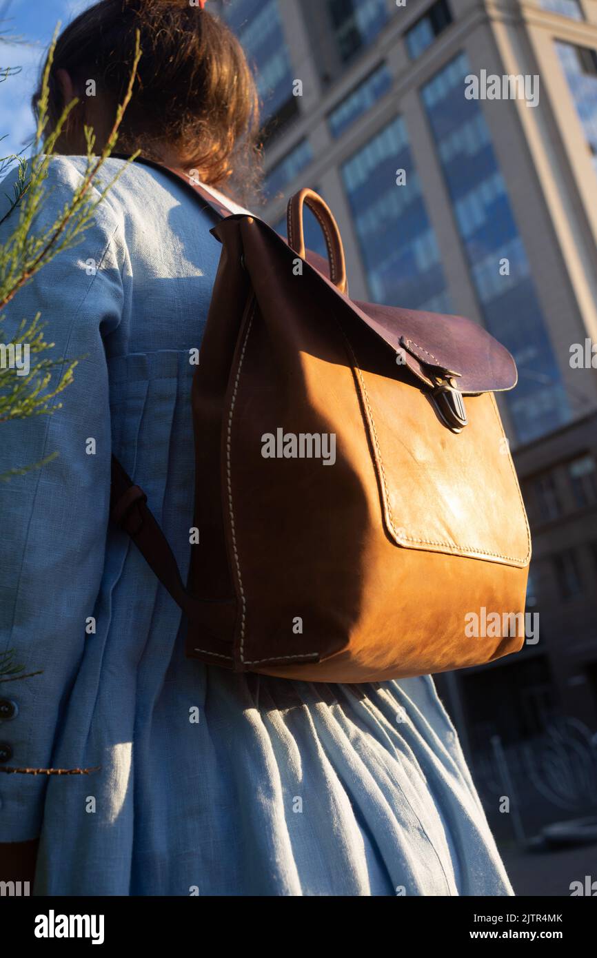 Girl in blue dress wears leather fashion handmade bag on the street. Leather backpack craft product. Kiev, Ukraine. Stock Photo