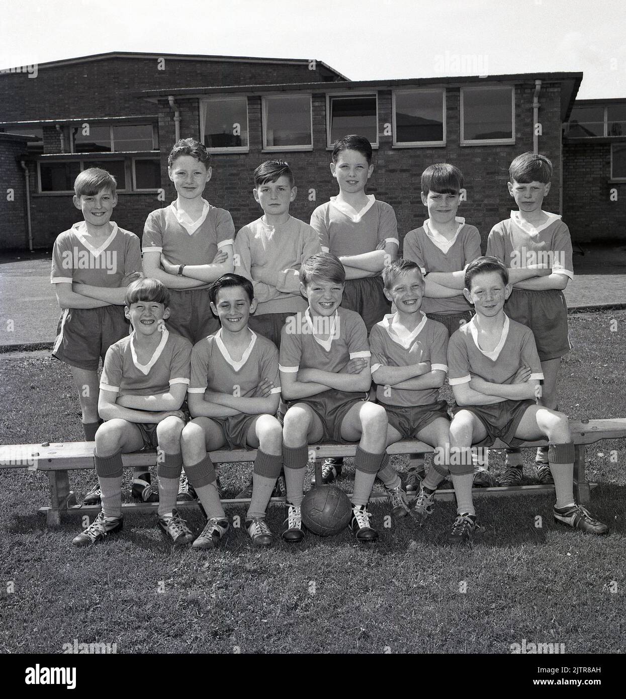 1965, historical, junior school football team group photo. Happy young boys wearing the kit and boots of the era; v- neck shirts, pull-string shorts and football boots, many with leather covered steel toepads including some with a high ankle. Seveal of the boys are wearing the popular 'Gola' boot of the day, a leather football boot, with a lower cut below the ankle, made by Botterill's of Bozeat of Northamptonshire, England, a boot company founded in 1895. In the 1960s, players of the famous Liverpool FC wore Gola football boots. Stock Photo