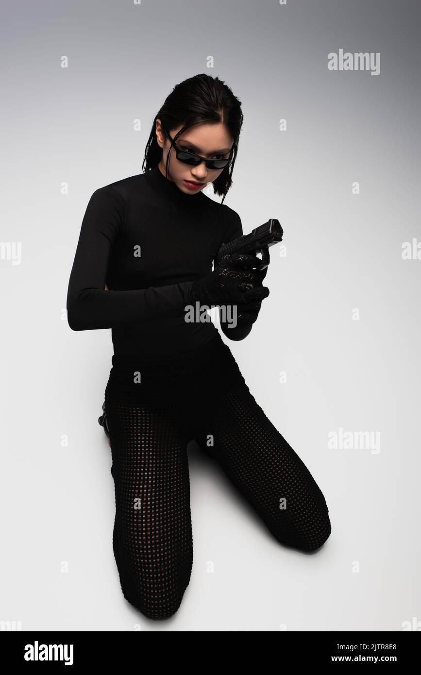 dangerous asian woman in total black outfit and stylish sunglasses holding gun on white,stock image Stock Photo