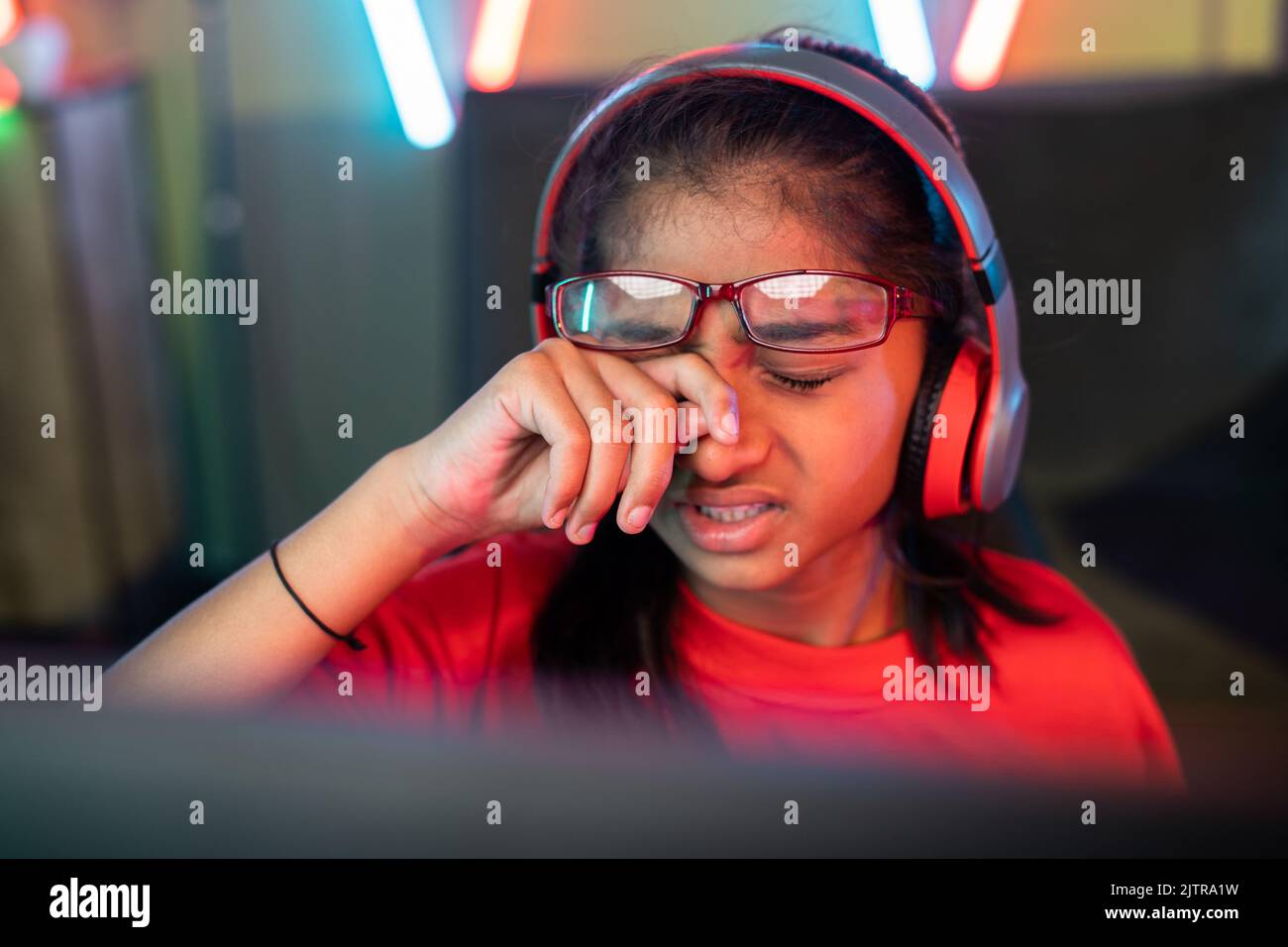 focus on hand, tired exhausted girl kid rubbing eyes by removing eyeglasses while playing online video game at home - concept of technology addiction Stock Photo