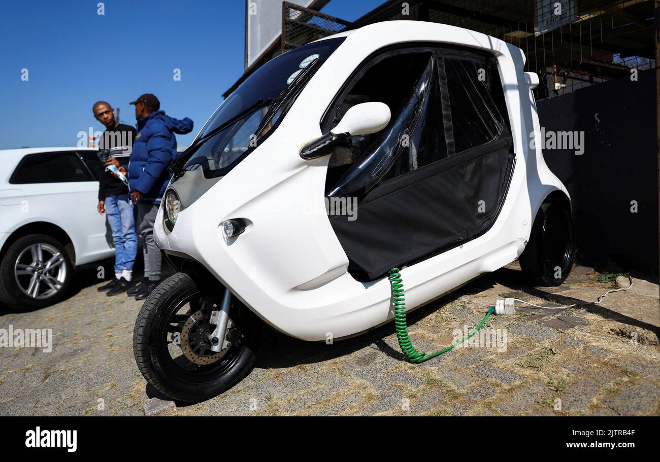 Locals chat as a three-wheel electric scooter is being charged using an electric power cable in Alexandra township, Johannesburg, South Africa, June 7, 2022. Picture taken June 7, 2022. REUTERS/Siphiwe Sibeko Stock Photo