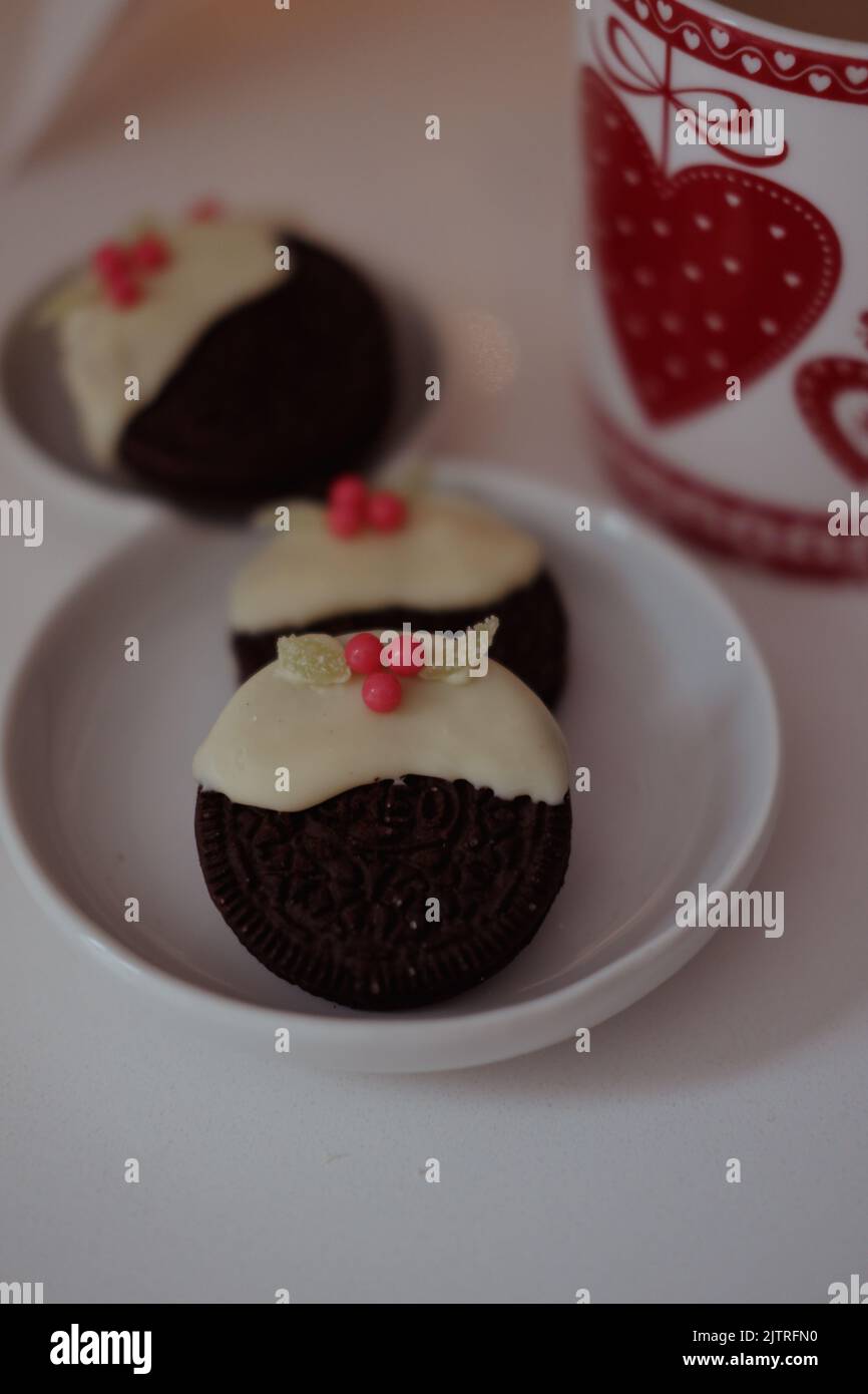 Chcocolate biscuits dipped in white chocolate and topped with candy/sweets to create mini Christmas puddings. Stock Photo