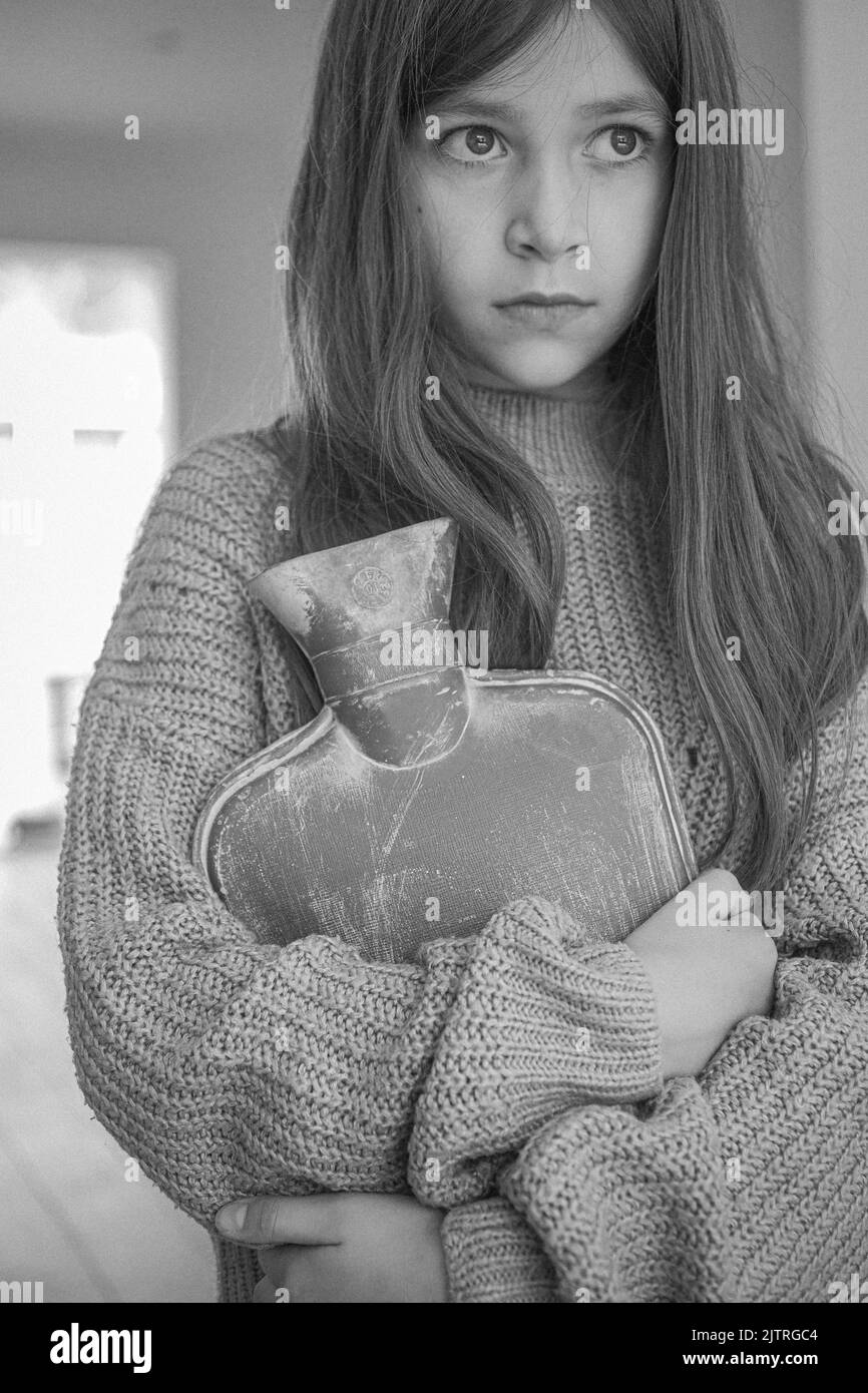 child holding a hot water bottle , trying to keep warm as fuel bills rocket Stock Photo