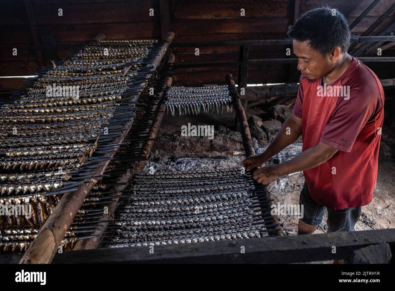 A fisherman arranges smoked fish at a grilling location in Lalimbue