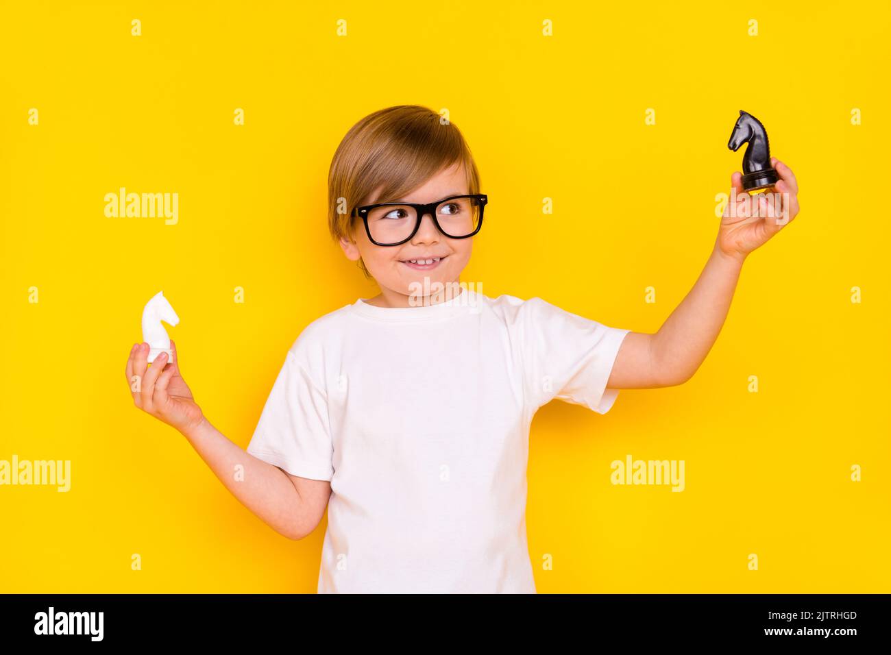 Portrait of handsome cheerful intellectual pre-teen boy holding chess figures playing move isolated over bright yellow color background Stock Photo