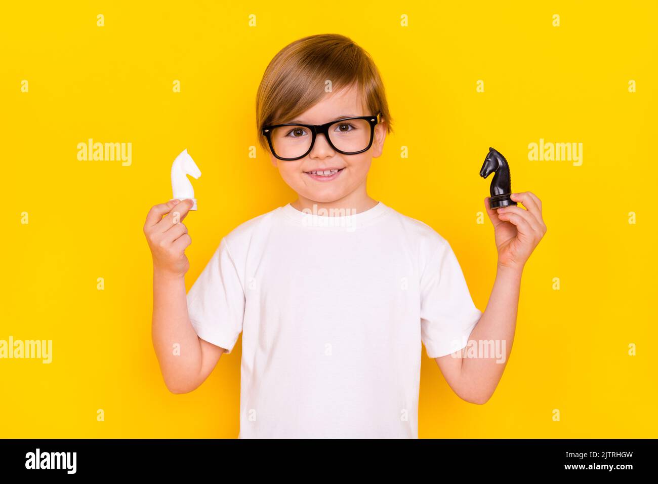 Portrait of handsome cheerful genius pre-teen boy schoolkid holding chess figures isolated over bright yellow color background Stock Photo