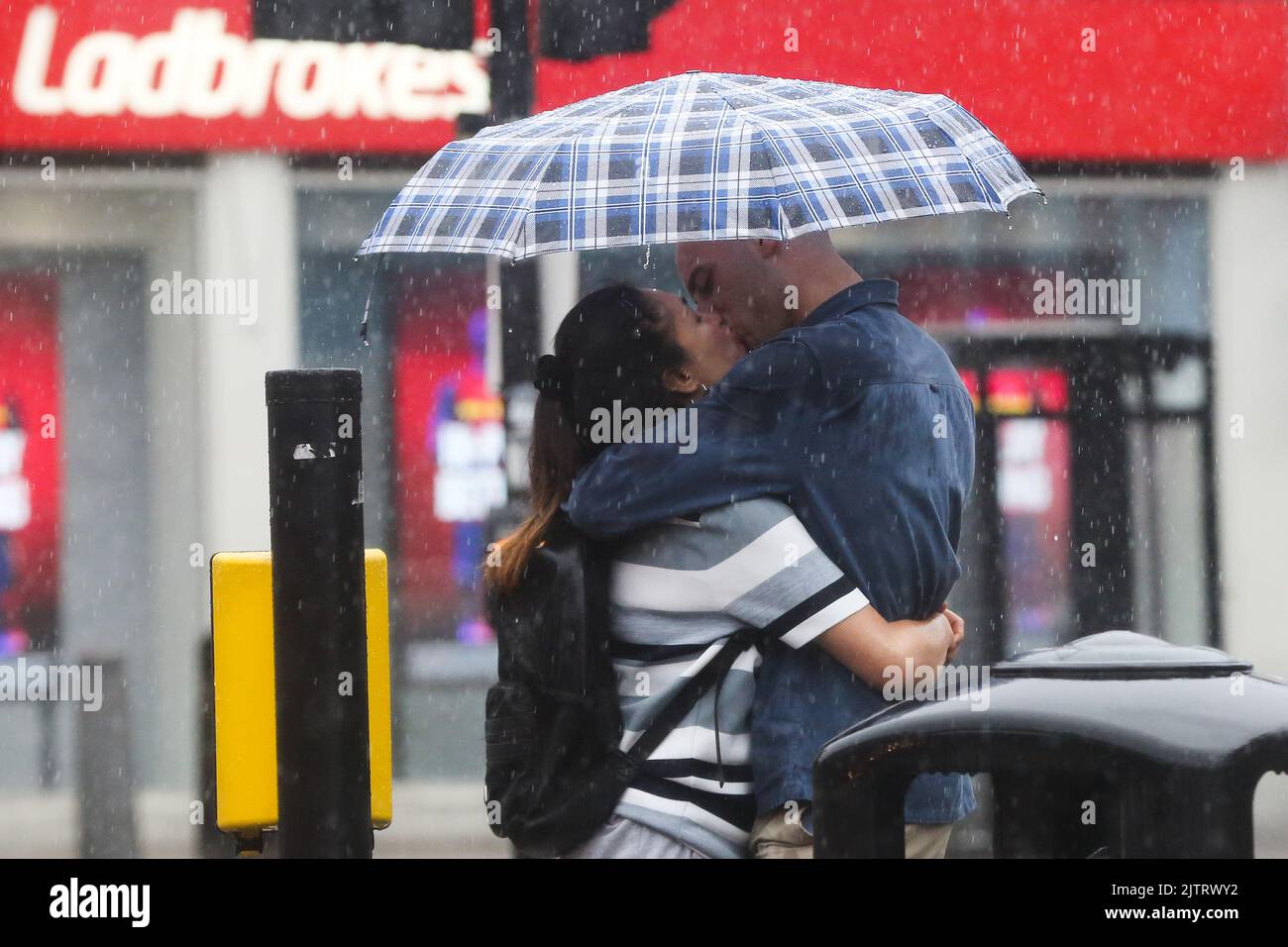 A Couple Seen Kissing While Sheltering Under An Umbrella During