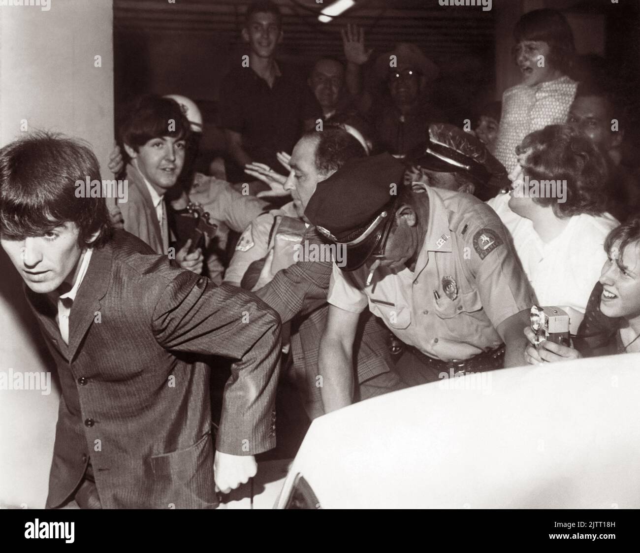 The Beatles (George Harrison in the foreground and Paul McCartney behind him) leaving the George Washington Hotel with police trying to control the pressing fans as the band headed for their Gator Bowl concert in Jacksonville, Florida, on September 11, 1964. (USA) Stock Photo