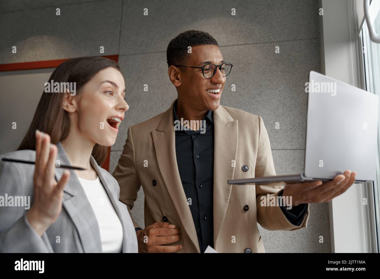 Two surprised business people working with laptop together standing near window Stock Photo